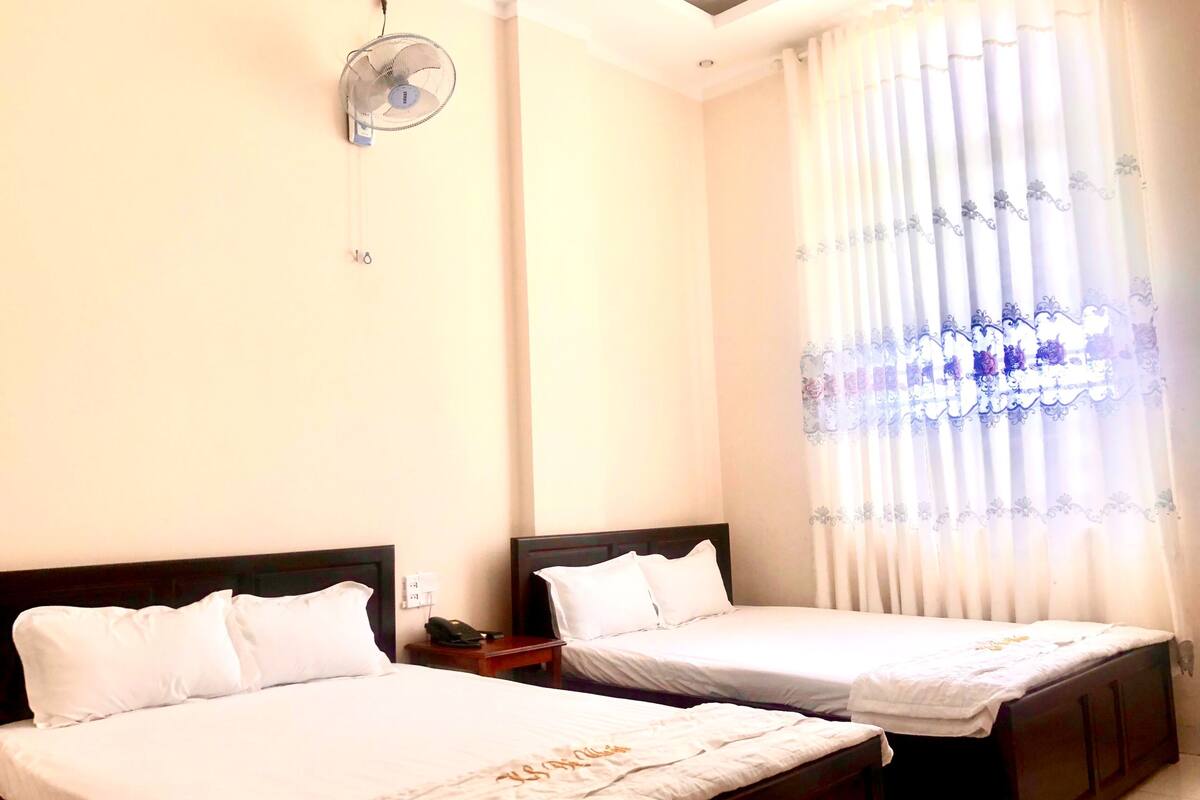 Ein Hotelzimmer mit zwei Einzelbetten, einem Nachttisch mit Telefon und einem Deckenventilator.