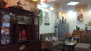 A living room with a dark wooden cabinet, a brown sofa, a glass display case, and a small table with a vase of flowers. - Hoa Hong Do Guesthouse (Xuan Huong - Da Lat)