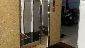 Un ascensor amb acabat metàl·lic, un panell de control amb una llum vermella i el reflex d'una moto al fons.