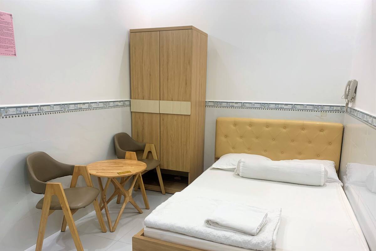 Una habitación pequeña y ordenada con una cama, dos sillas, una mesita y un armario.