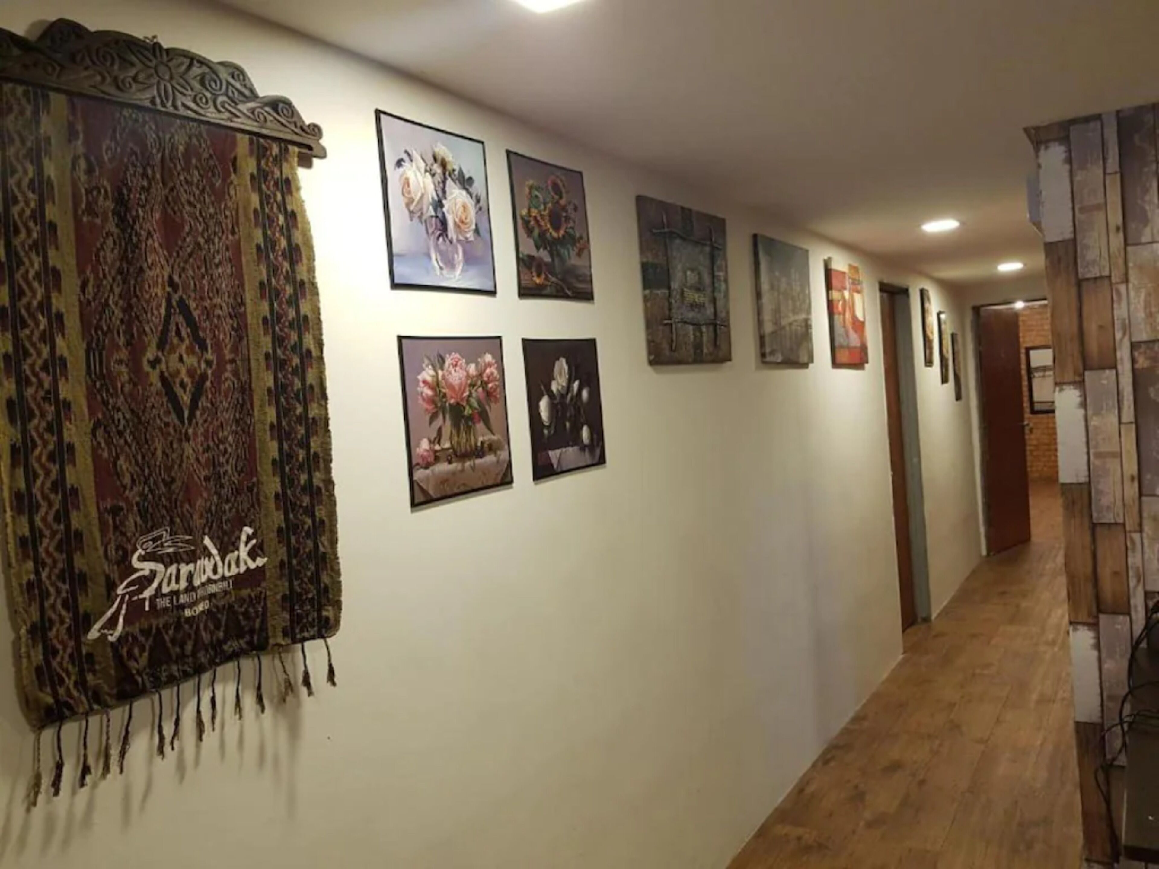 A hallway with a patterned tapestry, floral paintings, and a wooden wall panel.