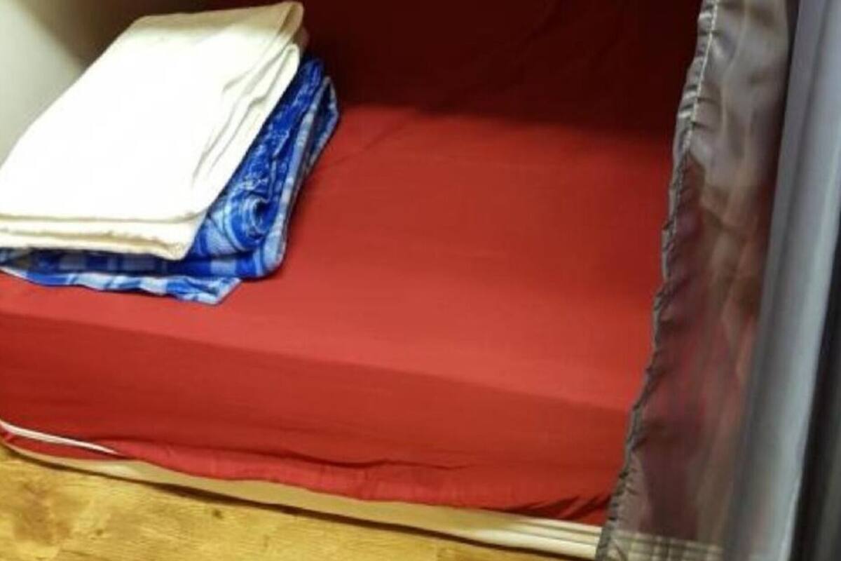 A small, single-bed room with a red mattress and a white blanket folded on the side.