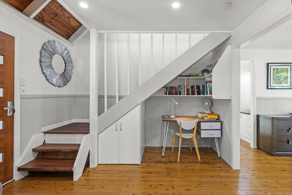 Una escalera conduce a una zona superior con un escritorio, una silla, estanterías y un espejo decorativo.