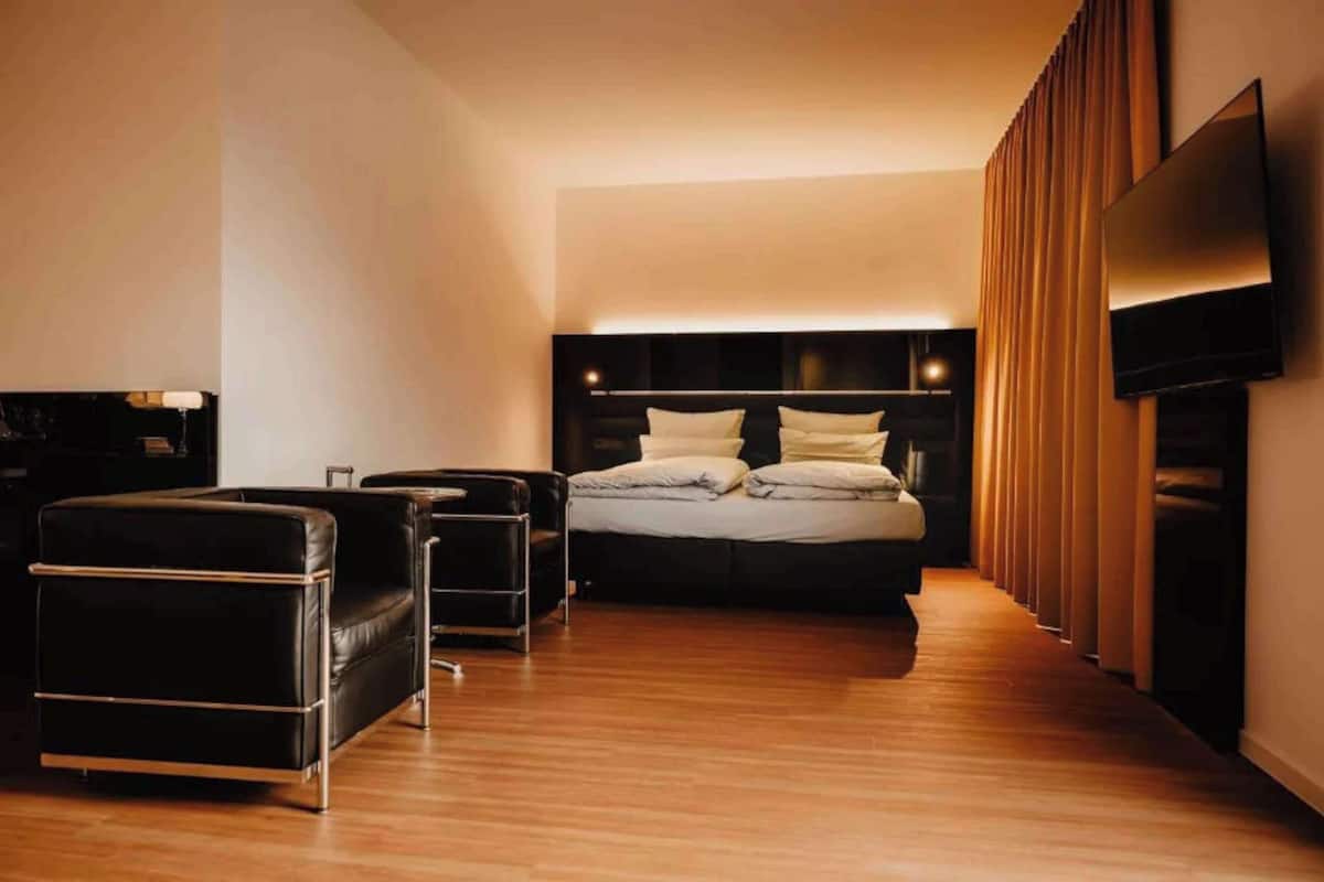 Ett modernt hotellrum med en stor säng, en svart lädersoffa, ett litet bord och en platt-TV som är monterad på väggen.