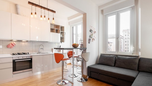 Une cuisine moderne avec des meubles blancs, un four encastré et un coin bar avec des tabourets.