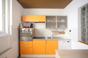 A kitchen with orange cabinets, a stainless steel oven, a coffee maker, and a dishwasher.