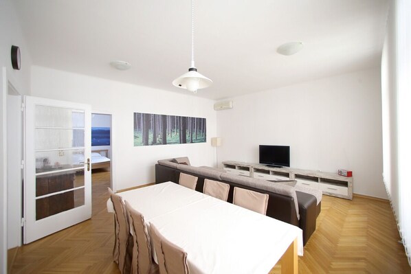 A modern, well-lit living room with a dining area, a sofa, a TV, and a painting on the wall.