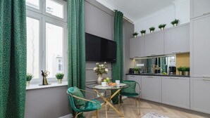 A modern kitchen with grey cabinets, a round glass table, and two green upholstered chairs.