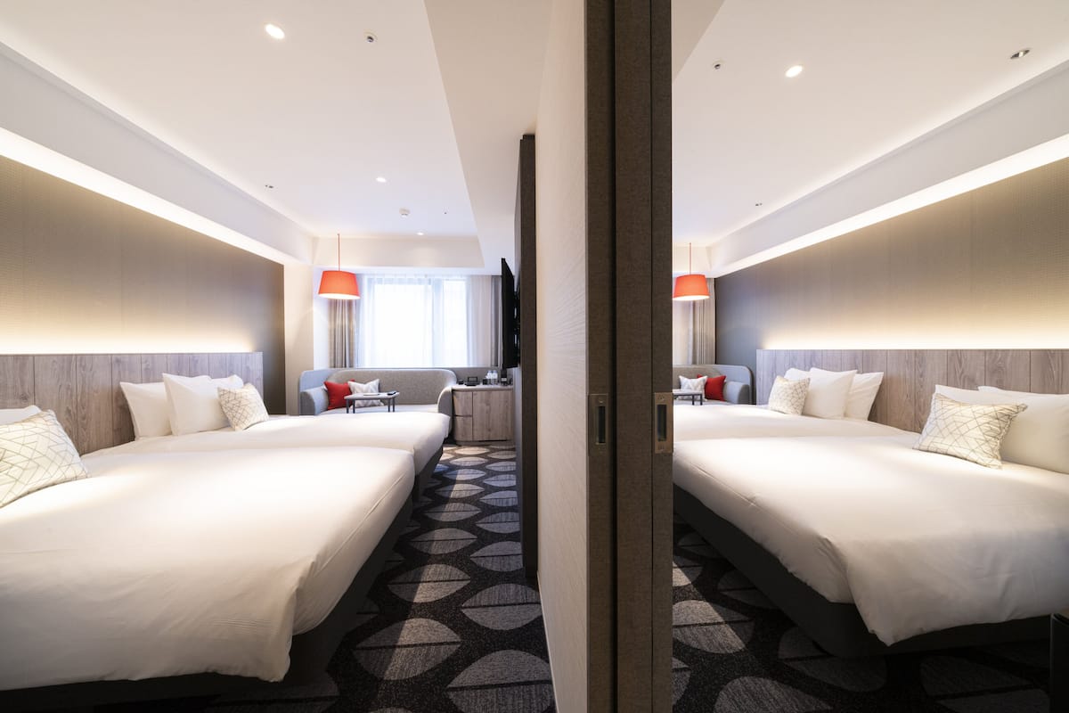 A hotel room with two beds, a desk, a chair, and a TV.