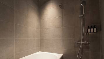A modern bathroom with a freestanding bathtub, a showerhead, and a small shelf with toiletries.