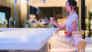 A woman seated at a bar with a drink, in a modern interior with pendant lighting and a view of the interior space. - Hotel JAL City Toyama (Toyama)
