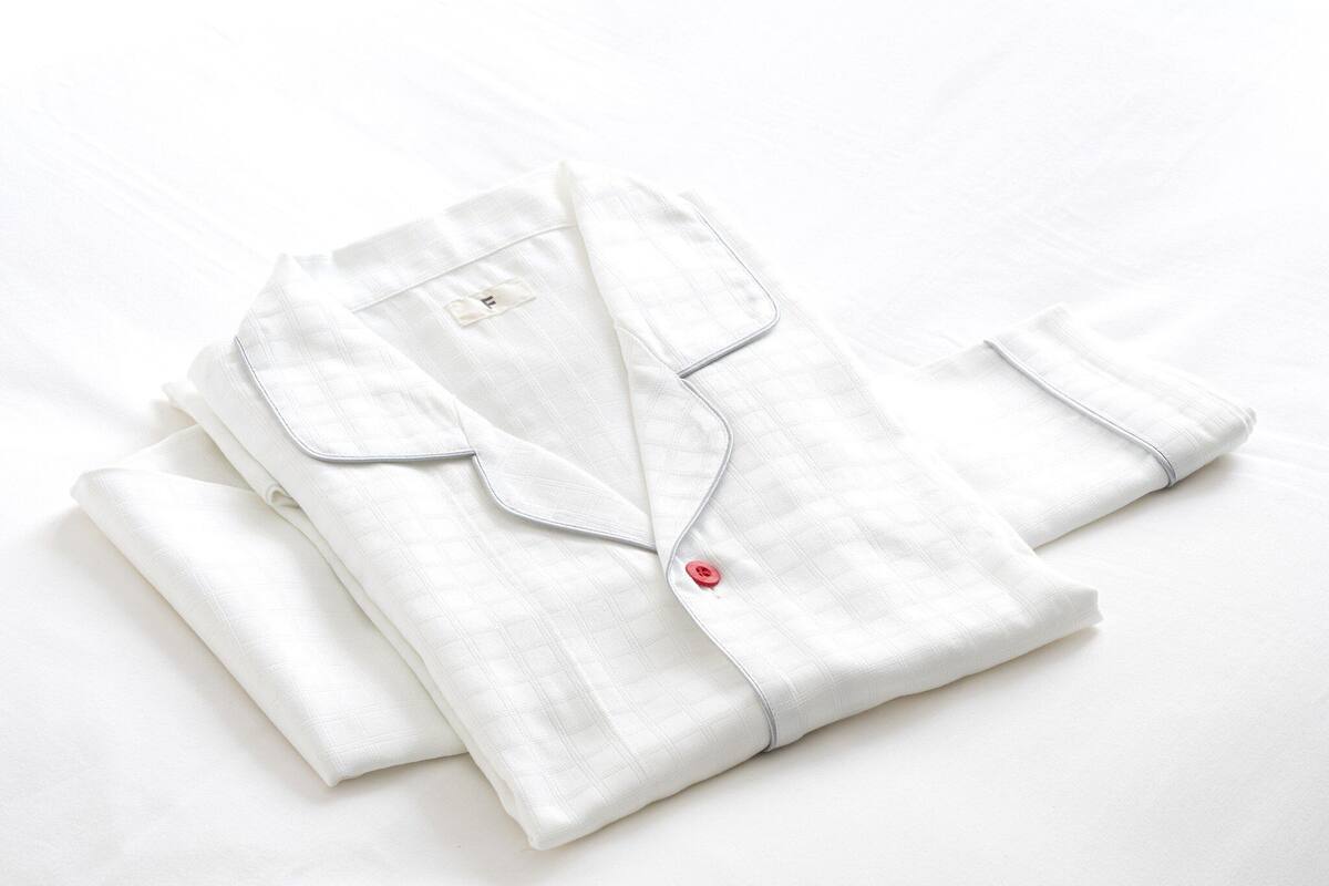 A neatly folded white shirt with a collar and button closure, placed on a white surface.