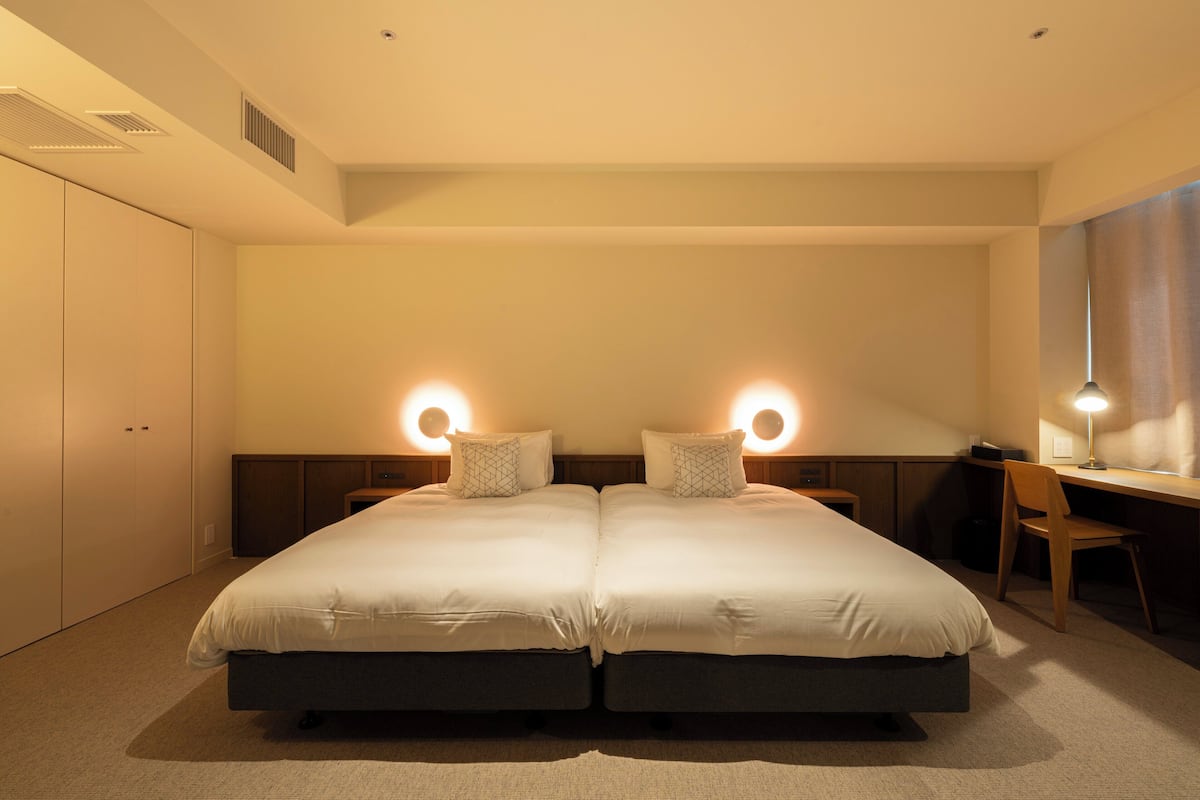 A double bed with two bedside tables, a desk with a chair, and a large window with curtains.