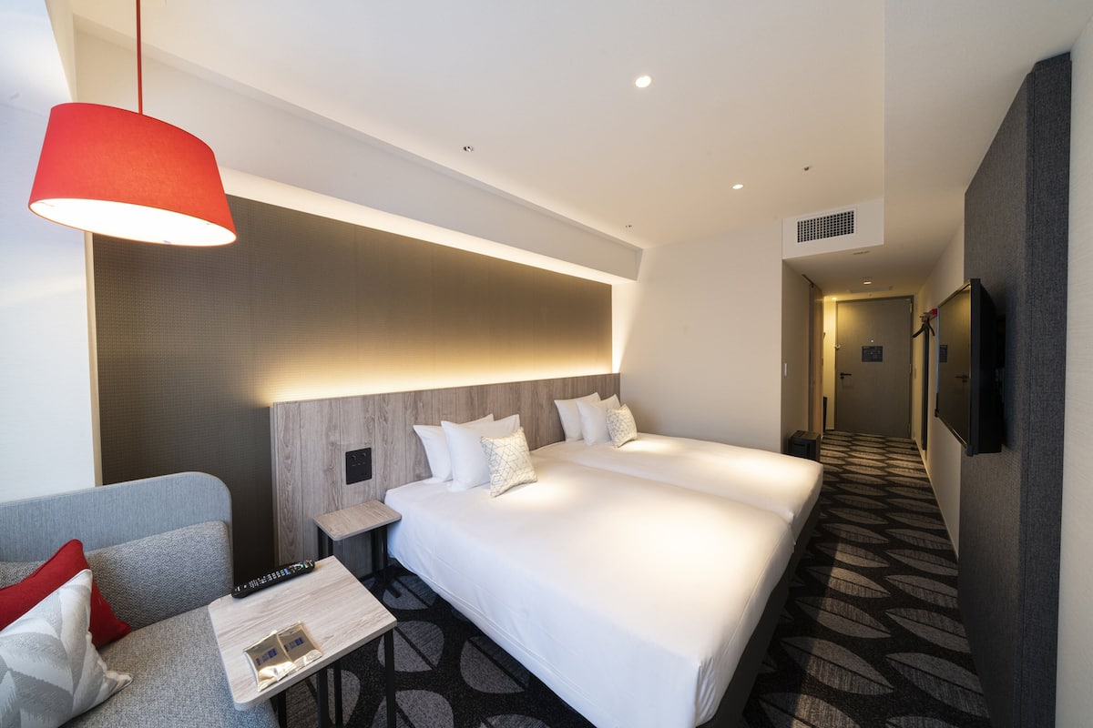 A hotel room with two beds, a sofa, a small table, and a red pendant light.