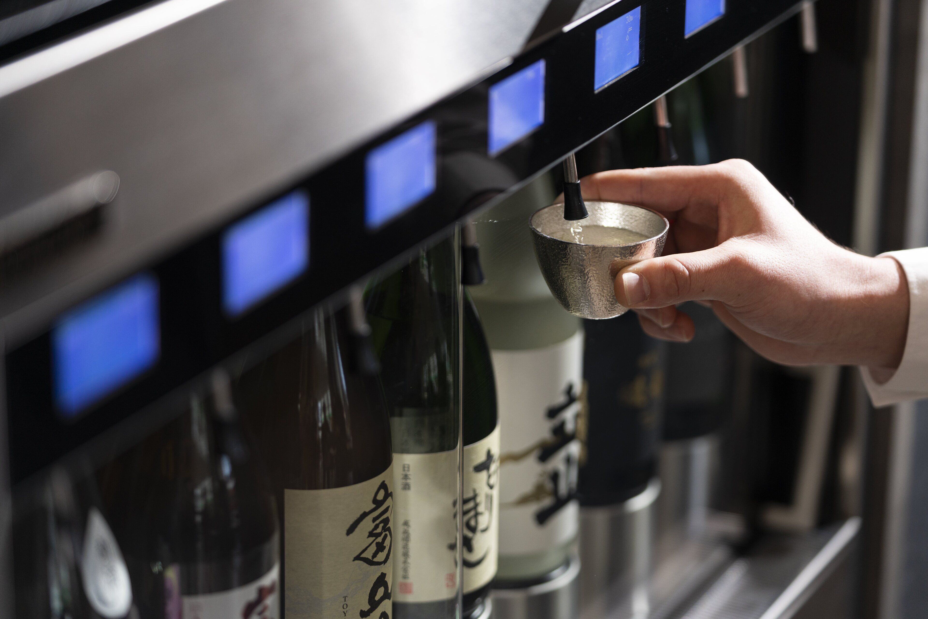A hand holding a metal cup under a shelf with bottles.