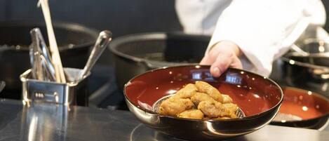 A chef holding a bowl of food, with a metal utensil holder and a pot in the background.