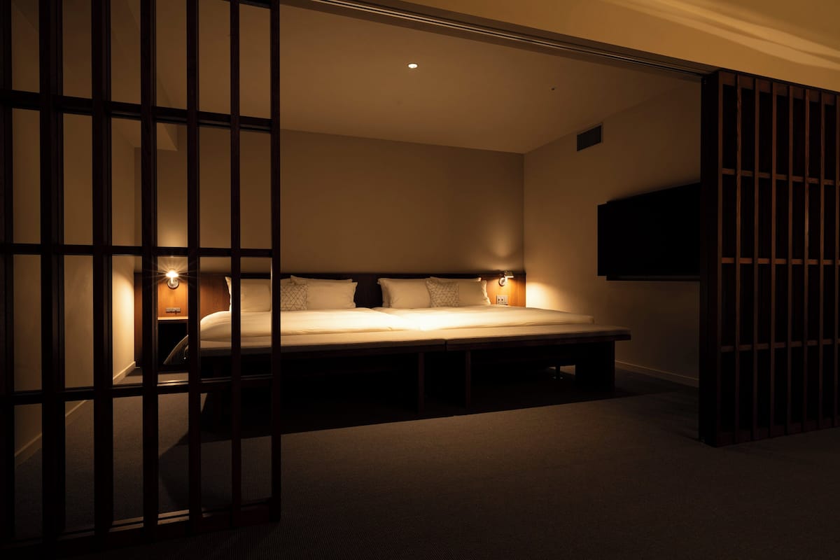 A bedroom with a bed, bedside lamps, a TV, and a sliding door.