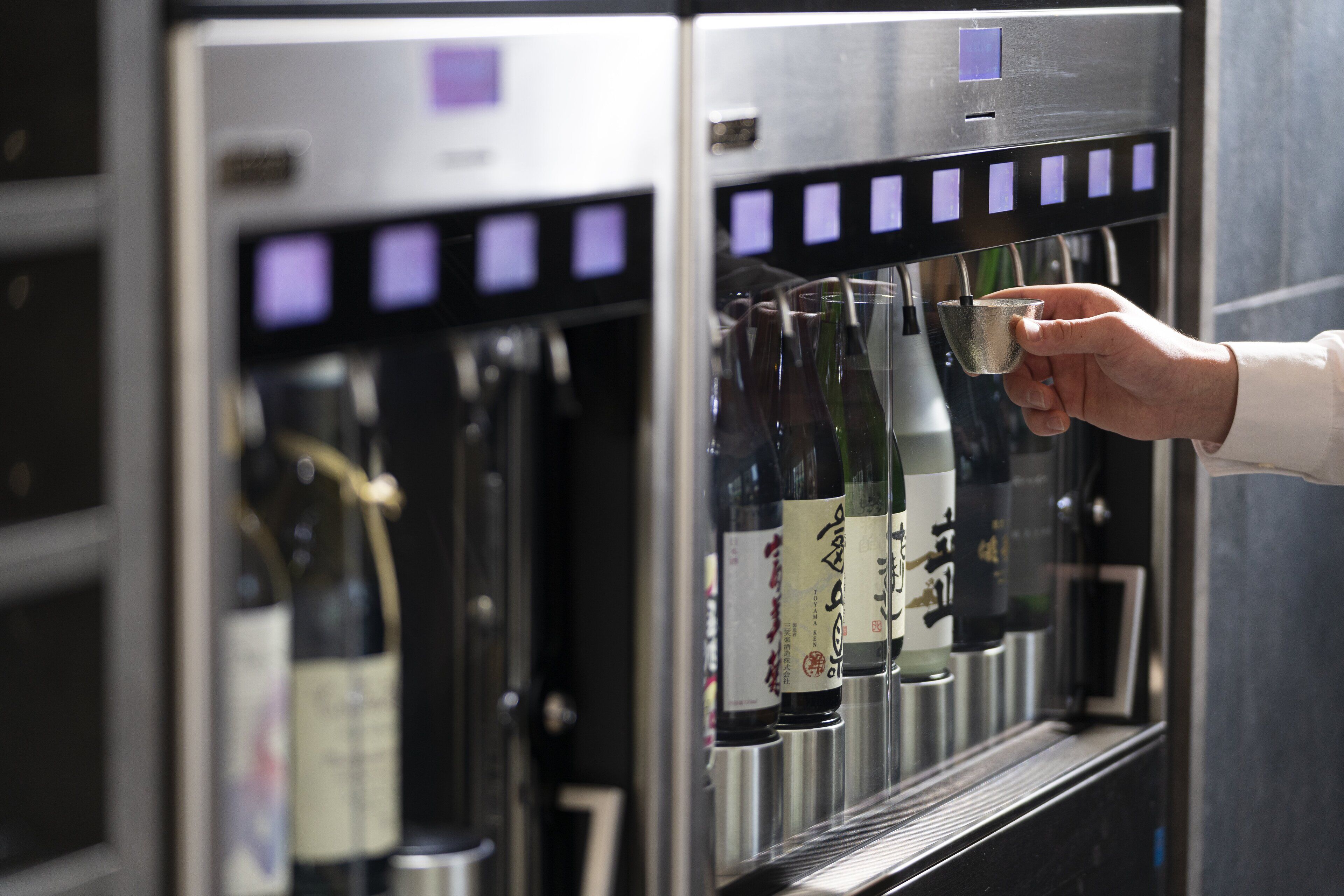 A hand selecting a wine bottle from a wine dispenser.