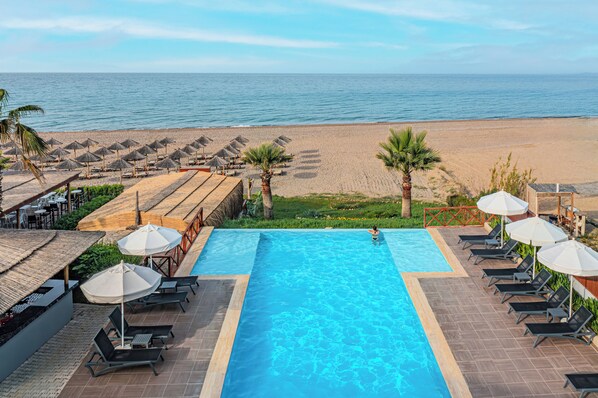 A pool area with lounge chairs and umbrellas, a beach in the background, and a clear view of the ocean. - Adora Calma Beach Hotel - Adults Only (Manavgat)