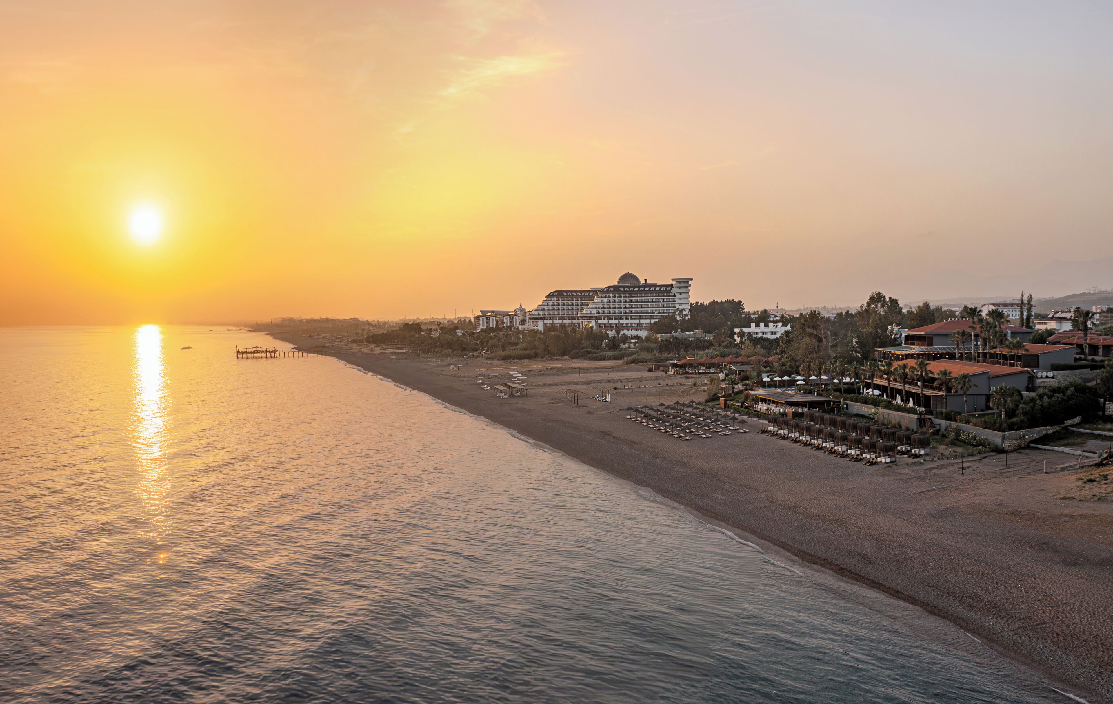 A beachfront hotel with a large building, a pier, and a beach area with sun loungers.
