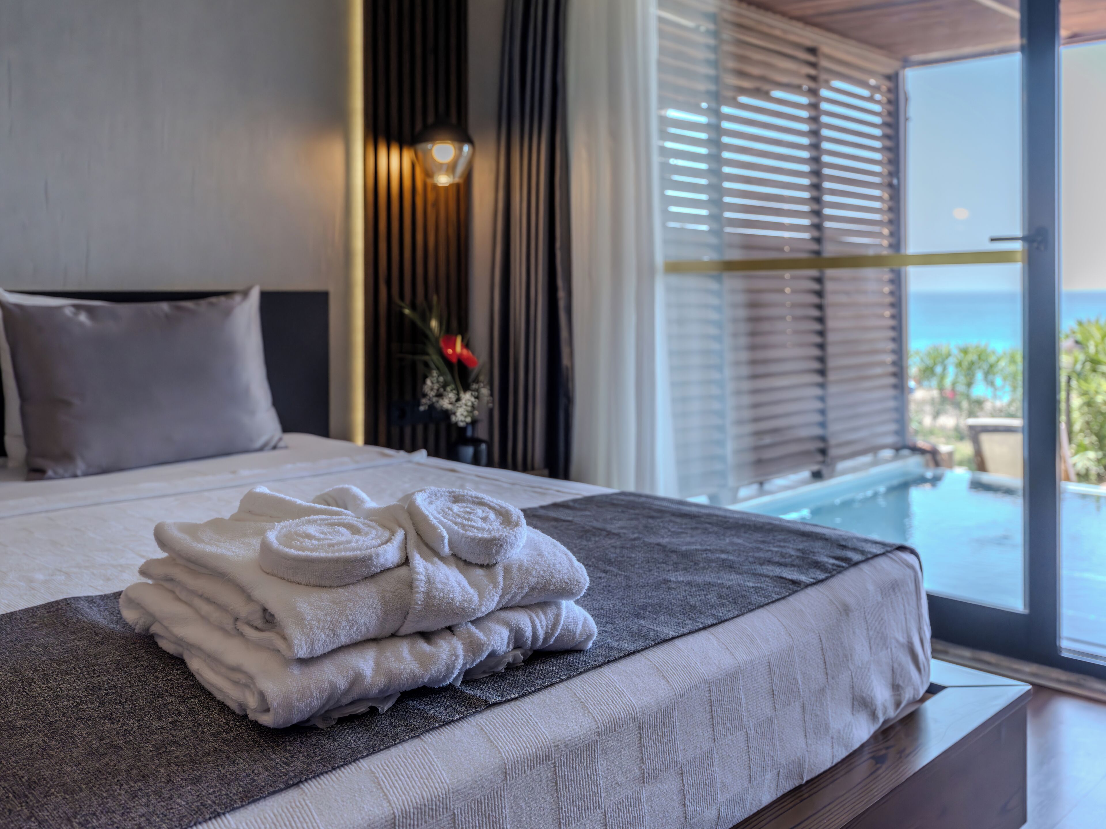 Una cama bien tendida con toallas, vistas al océano a través de amplios ventanales y un diseño interior moderno.