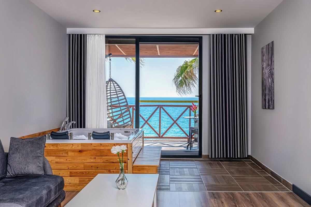 Un salón moderno con vista al mar, un sillón colgante y un sofá de madera.