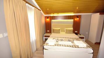 A hotel room with a large bed, bedside tables, a wooden ceiling, and wall-mounted lighting.