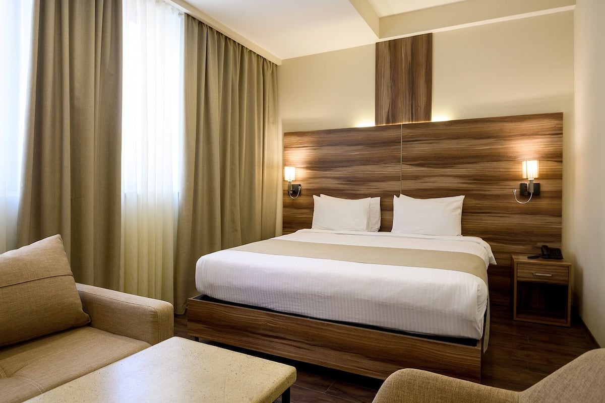 Habitación de hotel con una cama grande, dos mesitas de noche, un sofá y una silla.