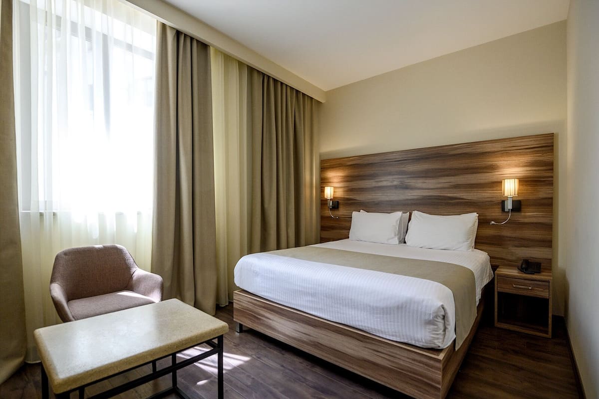 Una habitación de hotel con una cama, una silla, una mesa y dos lámparas de noche.