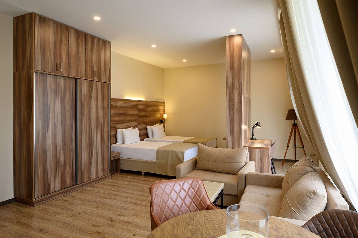 Habitación de hotel con un armario de madera, dos camas, un sofá, una mesita y una lámpara trípode.