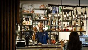 A bar area with shelves stocked with various liquor bottles, a bartender, and a customer. - Nacho Hotel Yerevan By One (Yerevan)