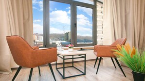 A modern room with two leather chairs, a small table, and a potted plant. A large window offers a city view. - Nacho Hotel Yerevan By One (Yerevan)