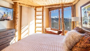 Una habitación acogedora con cama, una escalera de madera, ventana con vista a la montaña, televisor y lámpara.