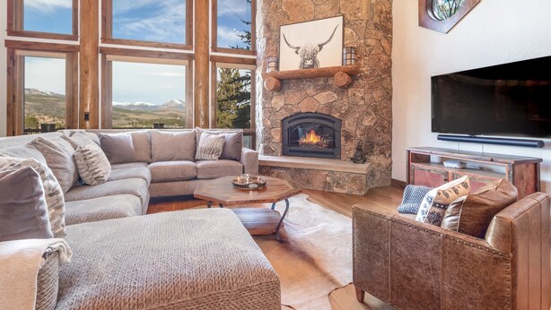 Ein gemütliches Wohnzimmer mit Kamin aus Stein, einem großen Flachbildfernseher und Bergblick durch große Fenster.