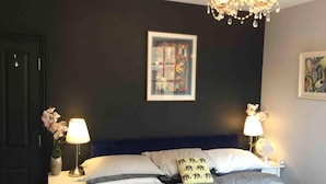 Un dormitorio con pared oscura, una cama con ropa de cama blanca, dos mesitas de noche con lámparas y un candelabro.