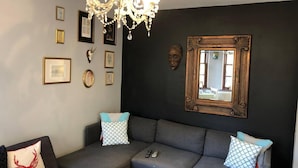 Una sala de estar con un sofá modular gris, una araña, obras de arte enmarcadas y un espejo en la pared.