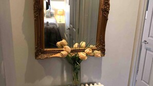 Un espejo con un marco ornamentado, un florero con flores y un radiador blanco.