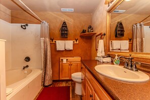 A bathroom with a bathtub, toilet, sink, and a large mirror.