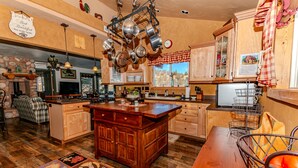Una cocina con armarios de madera, una isla central, ollas colgantes, una chimenea de piedra y un ventanal con vistas.