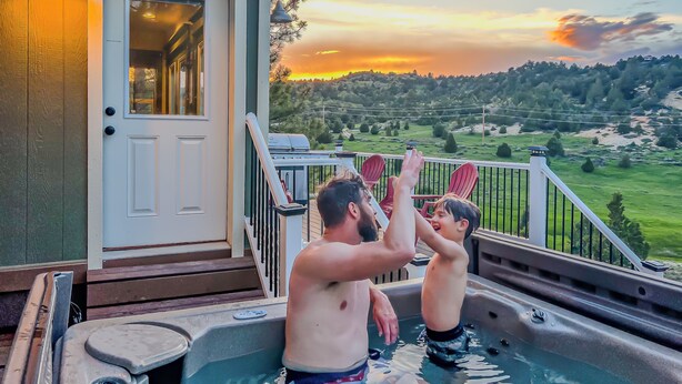 Un jacuzzi en una terraza con vistas a un atardecer y colinas al fondo.