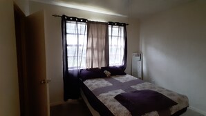 Una habitación pequeña con cama individual, ventana, mesita de noche y tocador.
