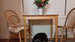 Una habitación con una mesa de madera y dos sillas, una pizarra y un florero con flores sobre la mesa.