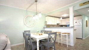 Un comedor con una mesa blanca y sillas grises, una cocina con armarios blancos y un reloj en la pared.