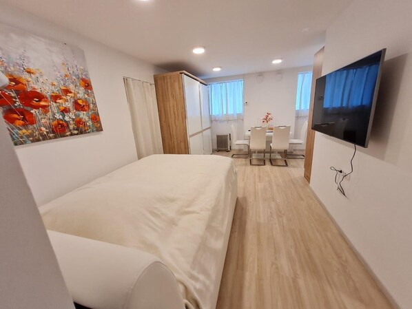 A modern hotel room with a bed, a desk, a chair, a TV, and a painting on the wall.