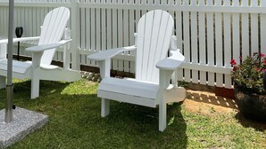 Un espace patio aménagé avec deux fauteuils Adirondack, une table et un grand parasol.