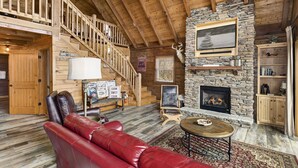 A log cabin interior with a stone fireplace, leather sofa, wooden staircase, and rustic decor. - Upscale Cabin With Stunning Views (Boone)