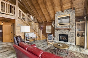 L’intérieur d’une cabane en rondins, avec une cheminée en pierre, un canapé en cuir, un escalier en bois et un décor rustique.