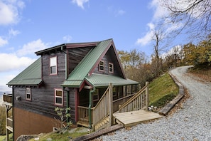 Une cabane en bois avec un toit vert, une terrasse en bois et une allée gravillonnée.