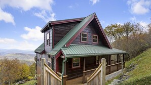 A wooden cabin with a green roof, a porch, and a staircase leading to the entrance. - Upscale Cabin With Stunning Views (Boone)