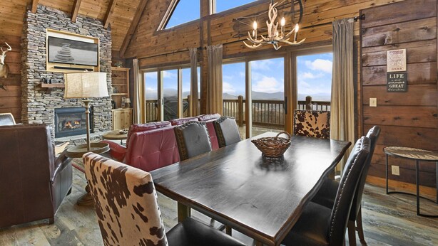A cozy log cabin interior with a stone fireplace, leather seating, and a large dining table. - Upscale Cabin With Stunning Views (Boone)
